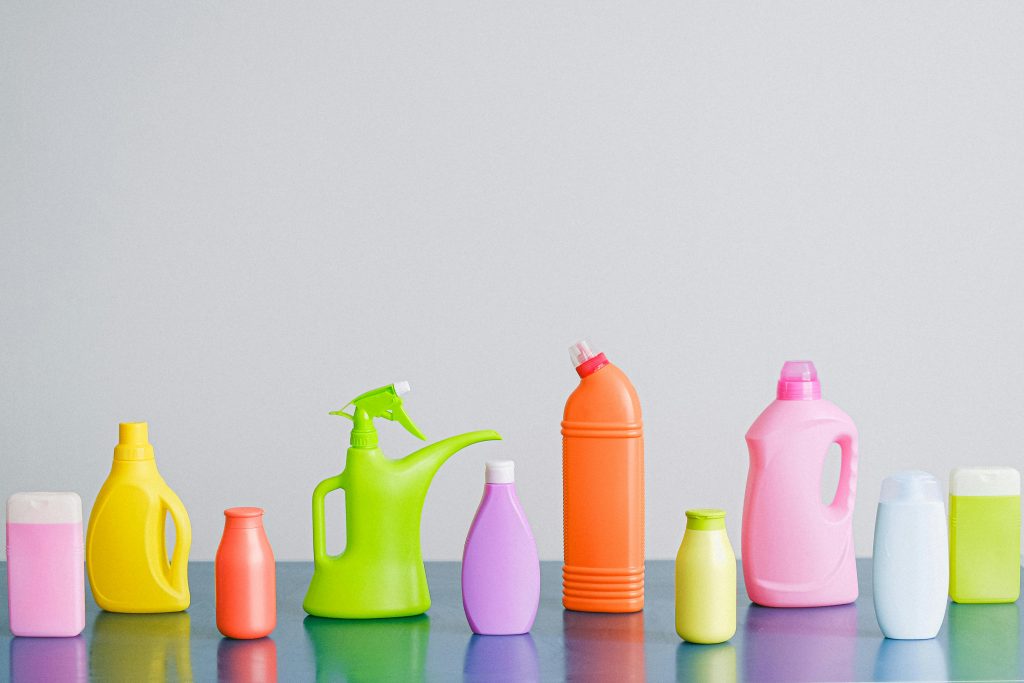 Arrangement of colorful plastic bottles with assorted cleaning products for household placed on table in row against white background in light studio
